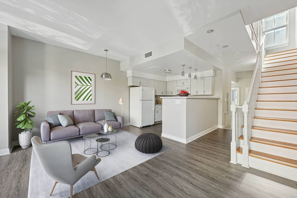 A living room with a grey sofa and a white kitchen in the background.