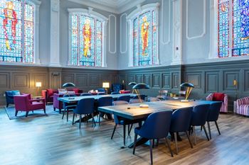 A room with tables and chairs and stained glass windows.
