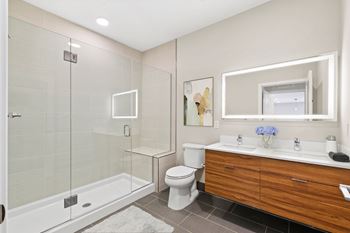 A modern bathroom with a glass shower stall, white toilet, and wooden vanity.
