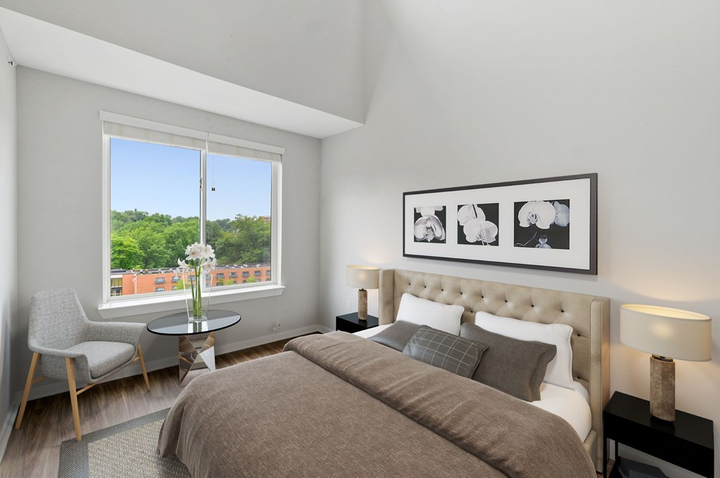 A bedroom with a large bed, a chair, a table, and a framed picture on the wall.