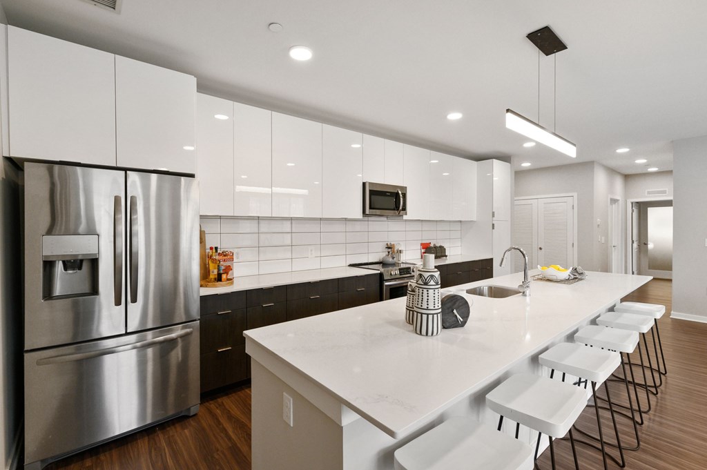 A modern kitchen with a long white counter and stainless steel appliances.