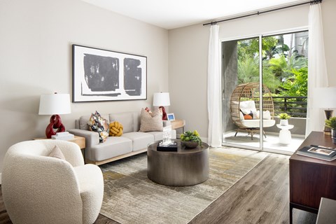 A living room with a grey sofa, a white chair, a round table and a painting on the wall.