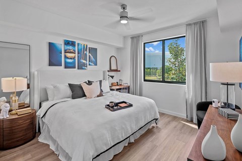 A bedroom with a large bed, a ceiling fan, and a view of the outdoors through a window.