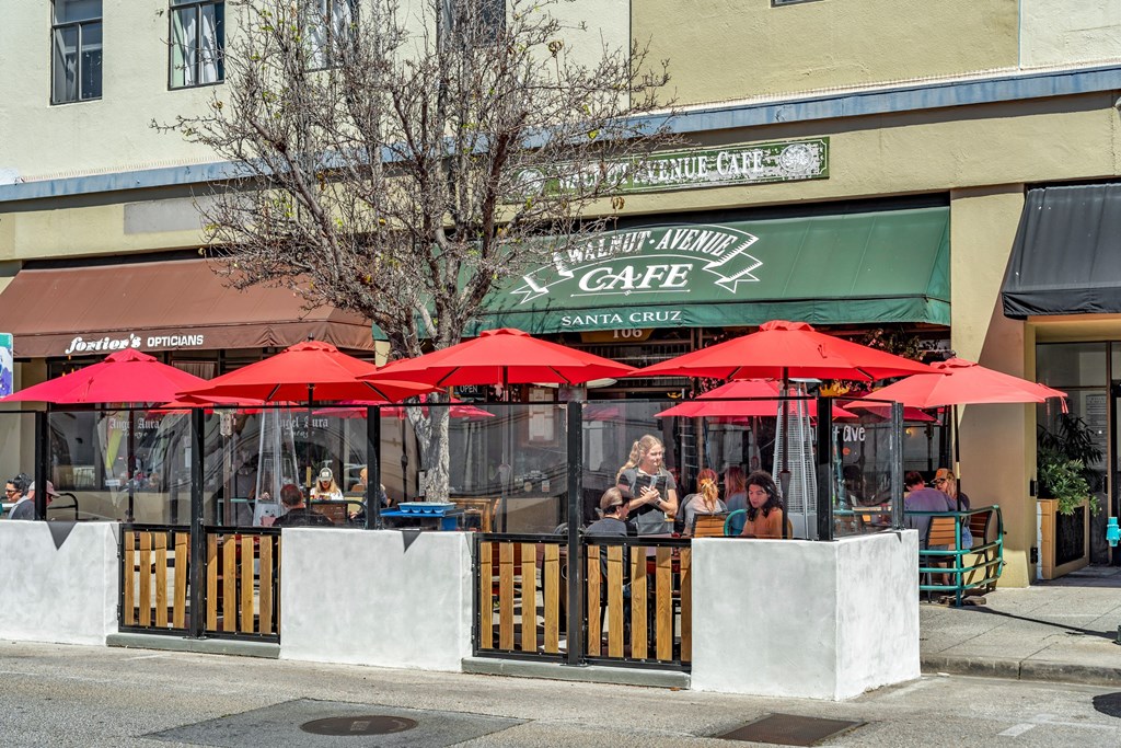 the exterior of a restaurant with red umbrellas and people sitting at tables