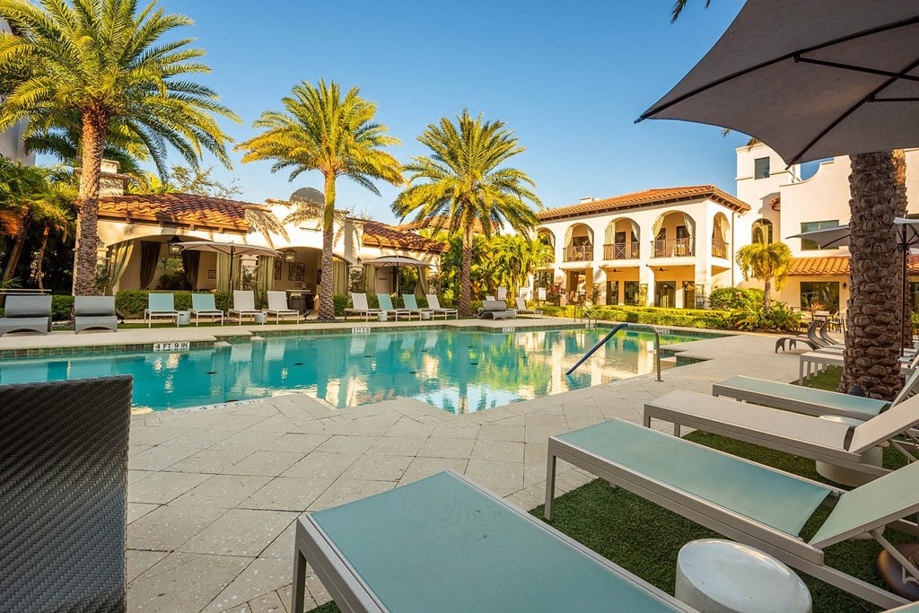 A pool surrounded by palm trees and lounge chairs.