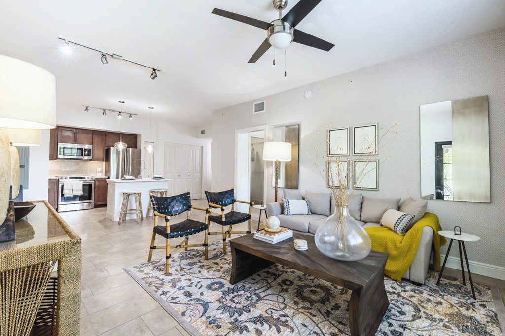 A living room with a rug, a sofa, a table, a chair, a vase, and a ceiling fan.