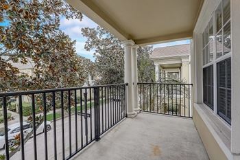 A balcony with a black railing and a view of a street with cars and houses.