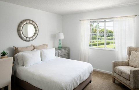 A bedroom with a large bed, a chair, and a mirror on the wall.