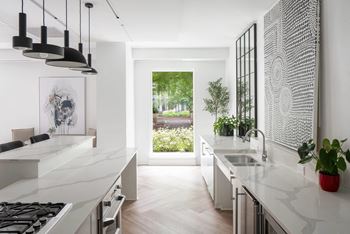 A modern kitchen with a large window overlooking a green area.