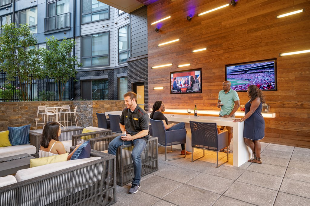 A man in a black shirt is sitting on a chair in a room with a wooden wall and a television screen.