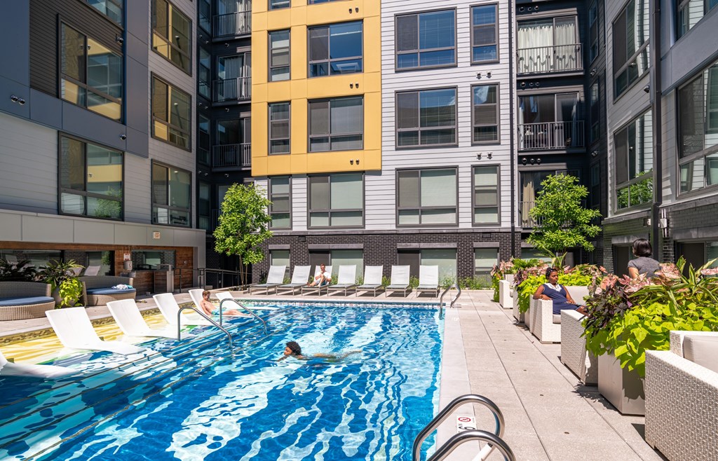 A person is swimming in a pool surrounded by chairs and plants.