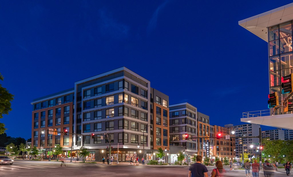 A city street at night with people walking and buildings with lit up windows.