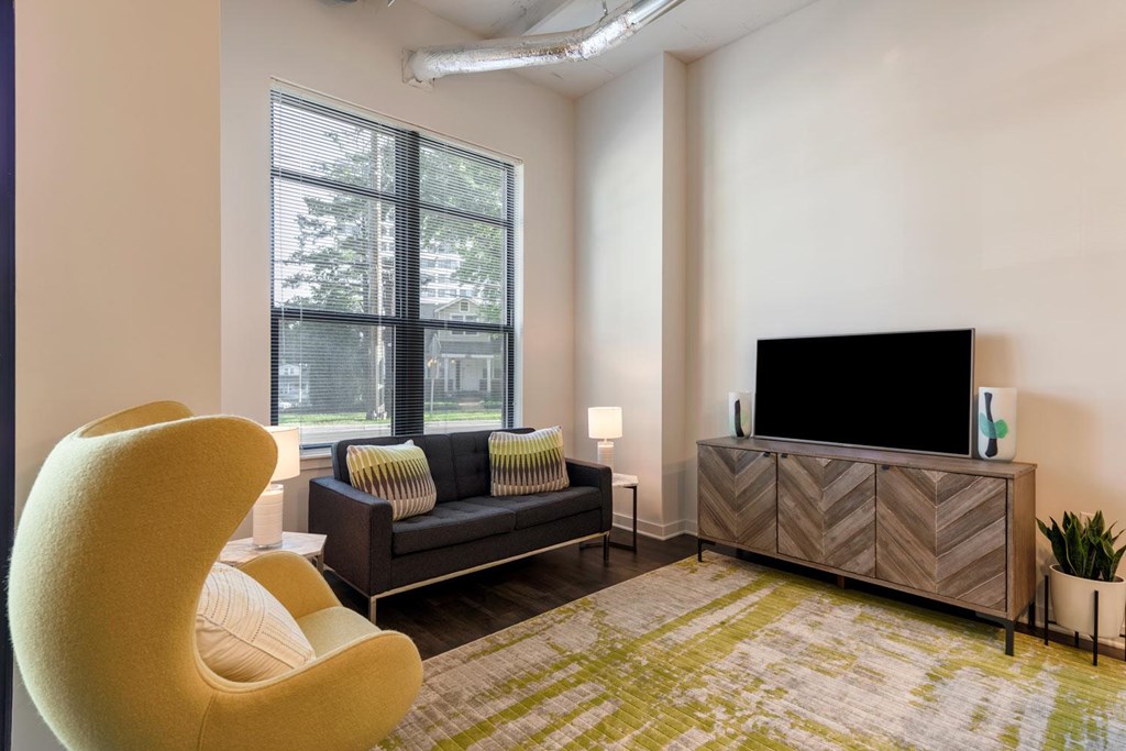 A living room with a yellow chair, a black couch, and a flat screen TV.