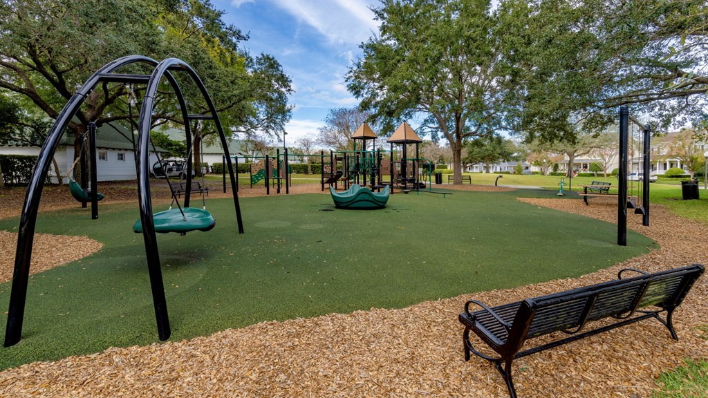 A playground with a green slide, a brown bench, and a yellowish ground.