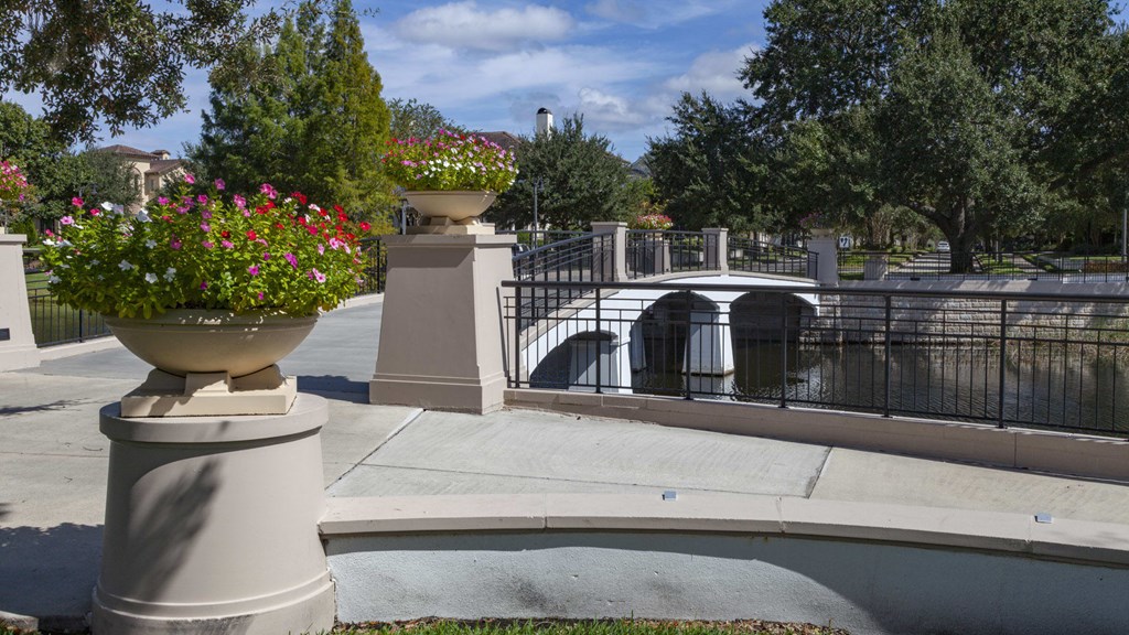 A bridge over a canal with a fence and a large planter with red flowers.