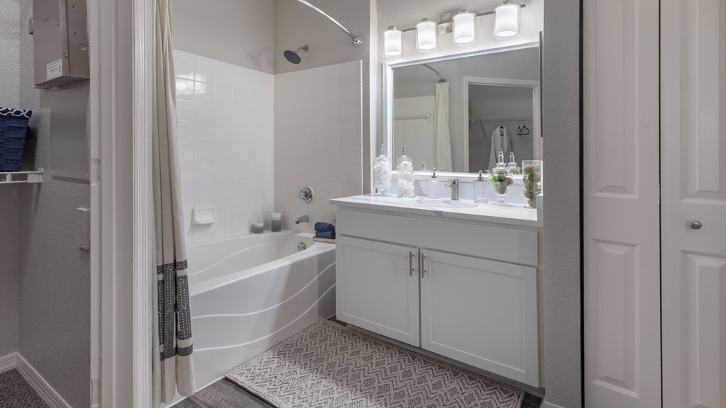 A white bathroom with a tub, sink, and mirror.