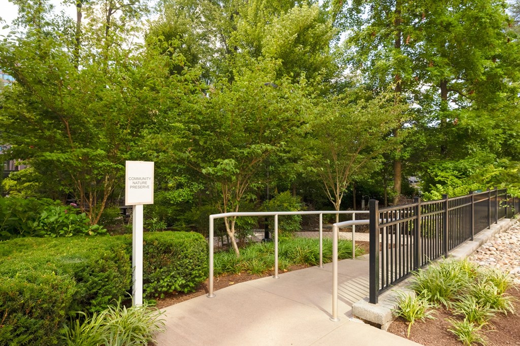 A white sign with black lettering on a post in front of a green bush.