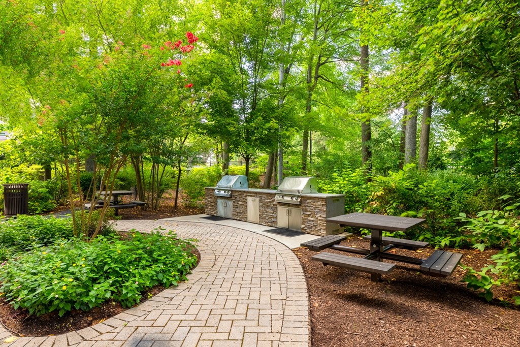 A park with a circular brick walkway, picnic tables, and a variety of trees.