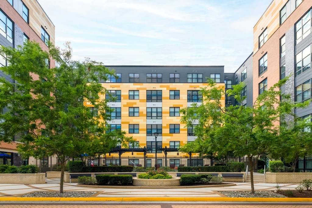 A modern multi-story building with a yellow and blue facade is surrounded by green trees.