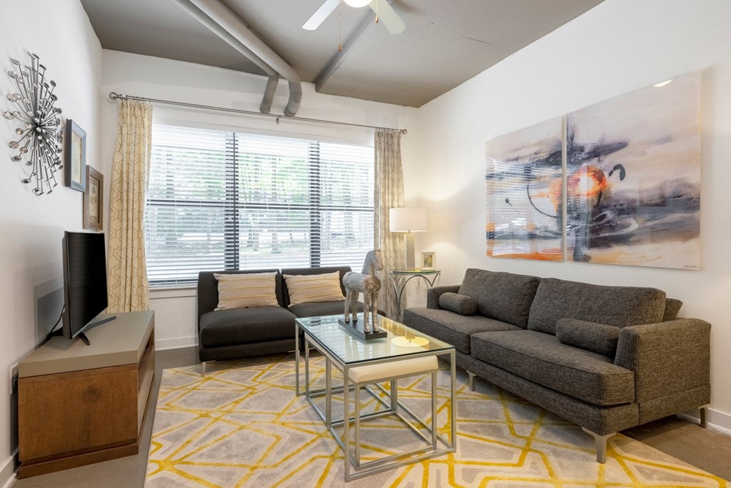 A living room with a grey couch, a glass coffee table, and a painting on the wall.