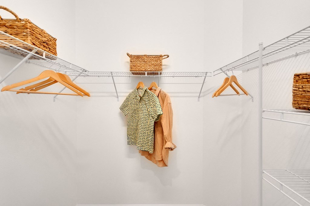 a walk in closet with a white wall and a closet organizer with clothes and baskets