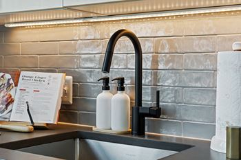 A kitchen sink with a black faucet and two white bottles on the counter.