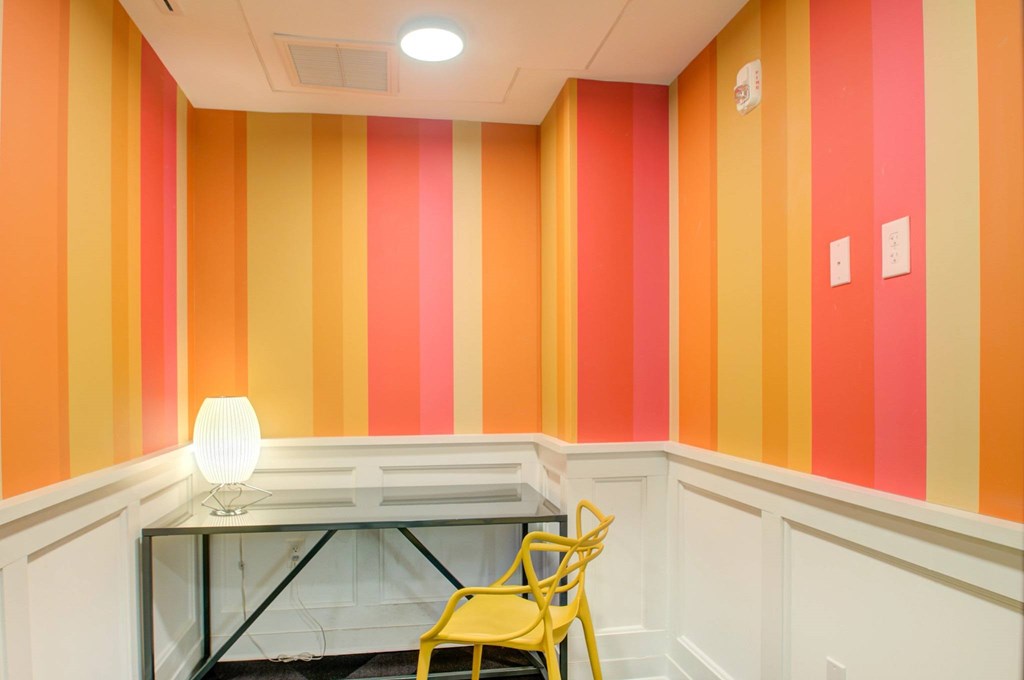 A yellow chair is in front of a desk with a lamp on it.