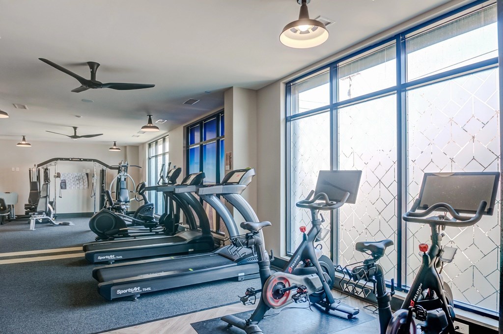 A gym with treadmills, exercise bikes, and a fan.