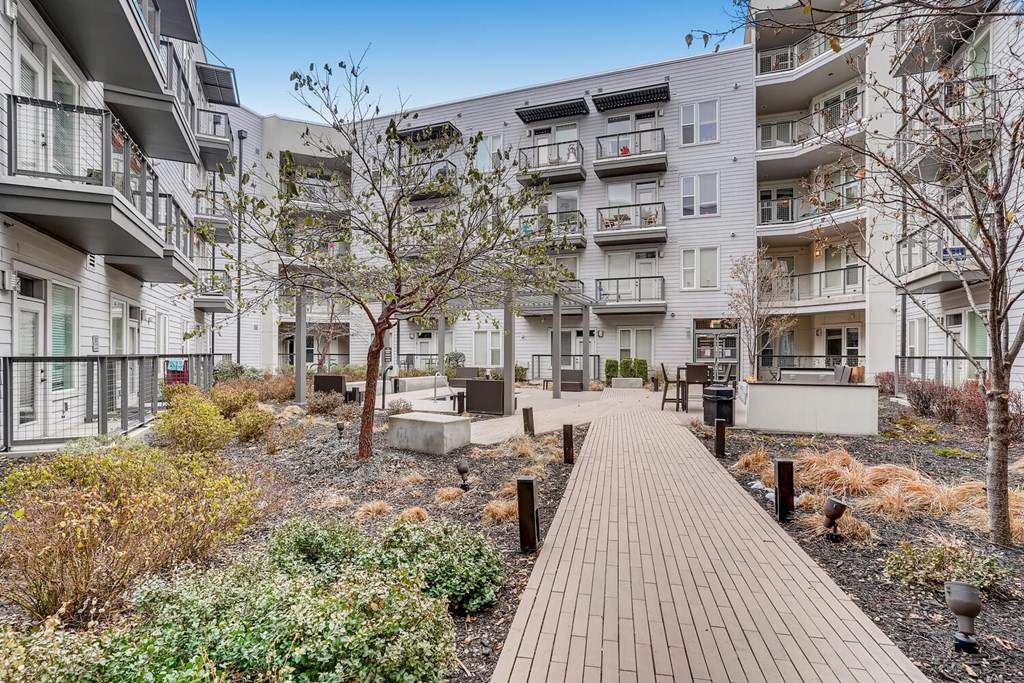 A long wooden walkway leads through a landscaped courtyard between apartment buildings.