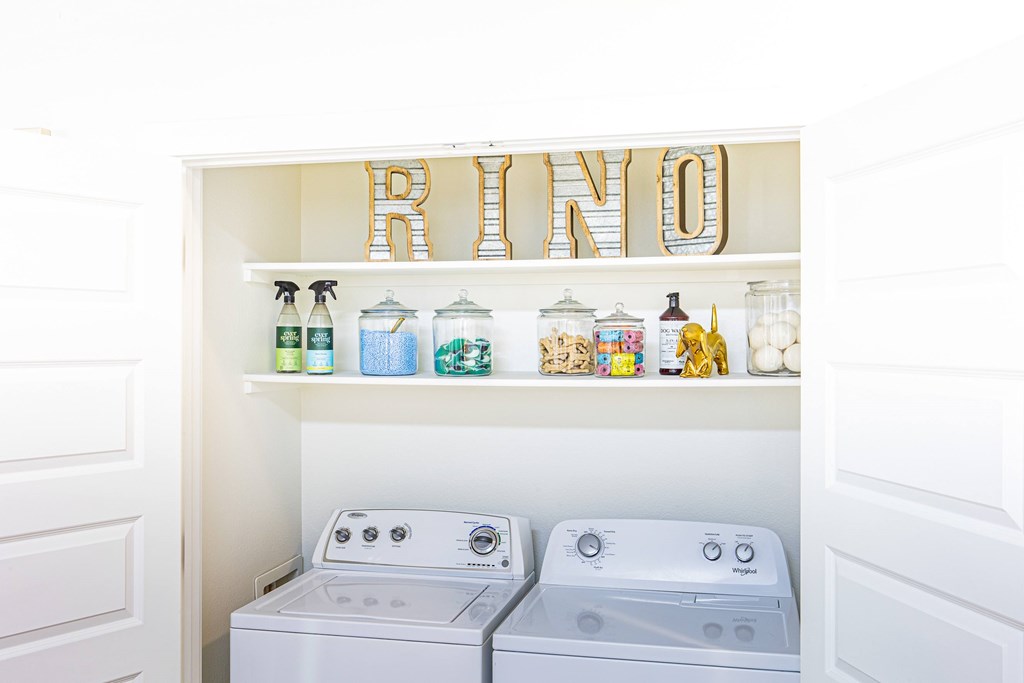 A white laundry room with a washer and dryer and a shelf with bottles and containers.