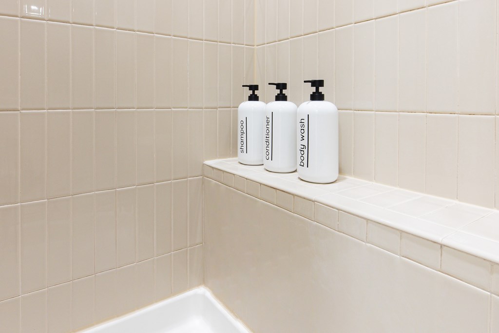Three bottles of hand soap and hand sanitizer on a shelf in a bathroom.