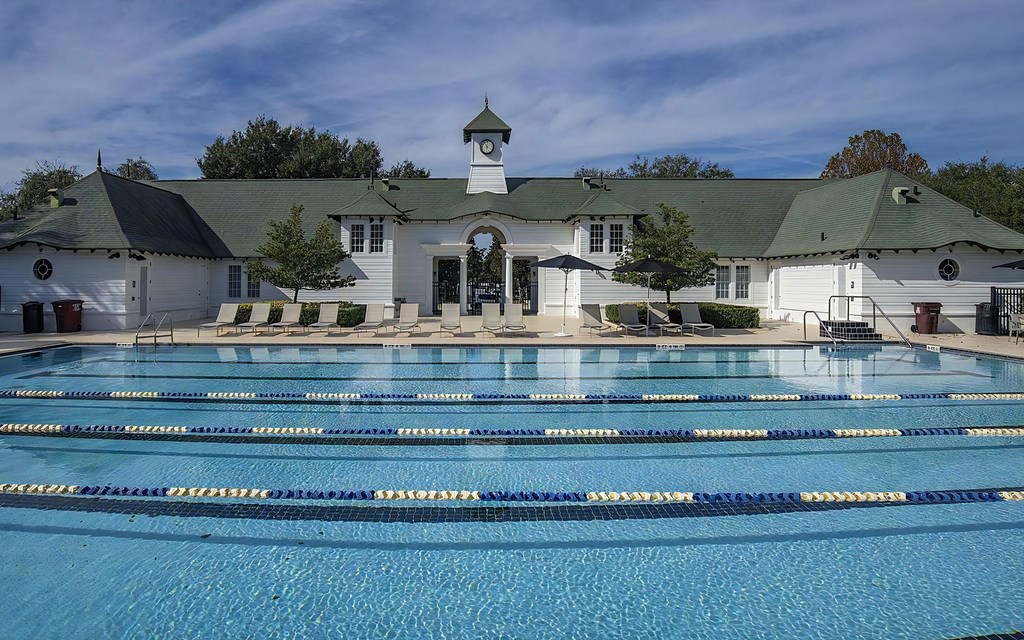 A large swimming pool in front of a white building with a green roof.