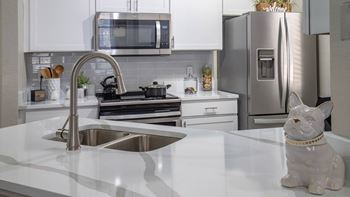 A white kitchen with a stainless steel refrigerator and a white cat figurine on the counter.