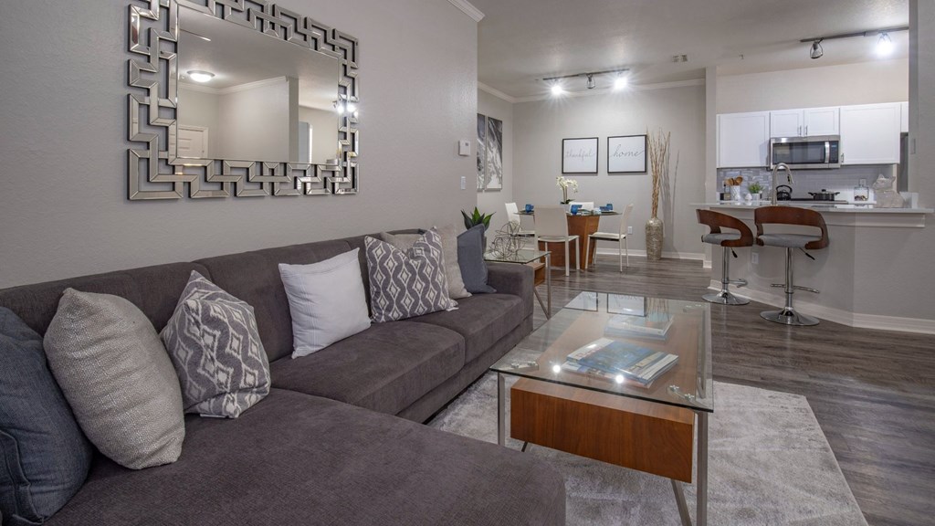 A living room with a grey couch and a mirror on the wall.