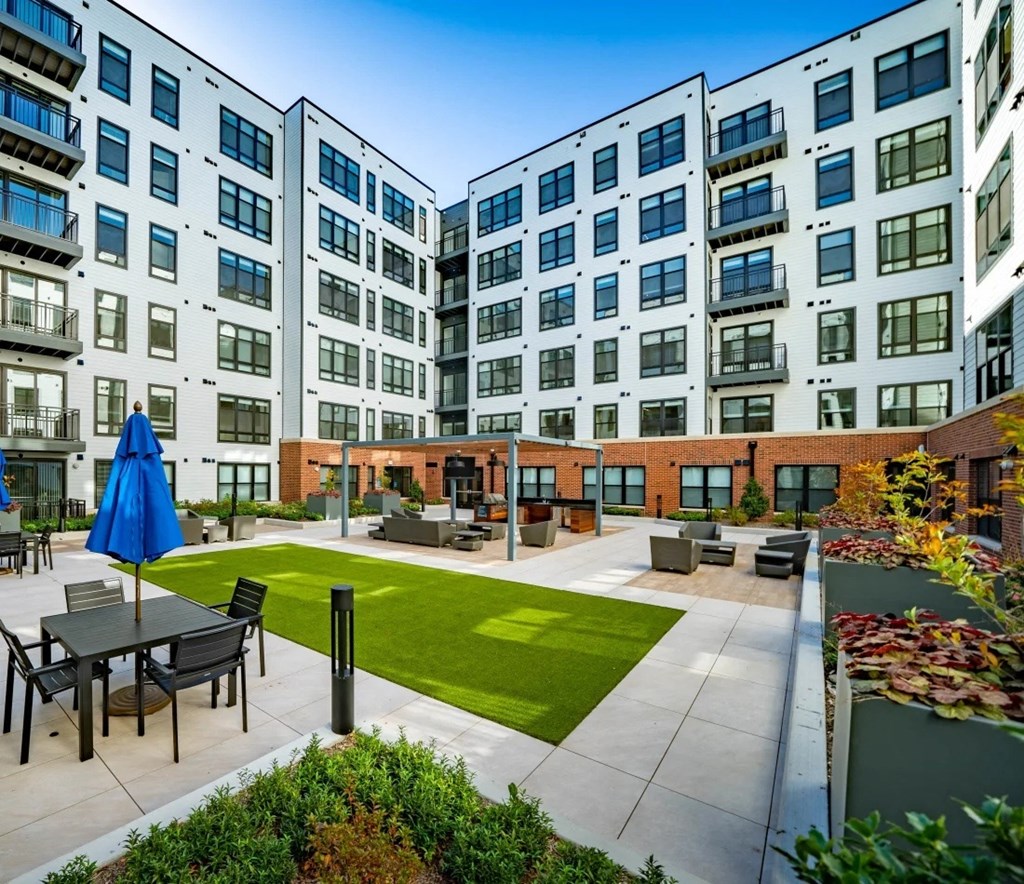 an outdoor courtyard with a lawn and tables in front of an apartment building
