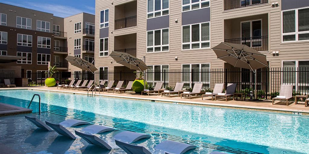 a swimming pool with chairs and umbrellas next to an apartment building