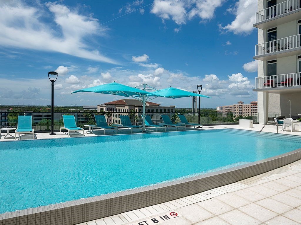 A pool with a blue umbrella and chairs.
