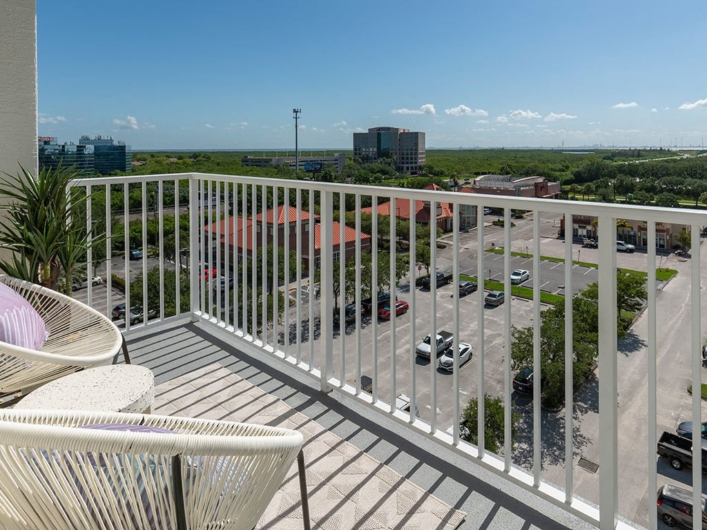 A balcony with a white railing overlooks a parking lot and buildings.