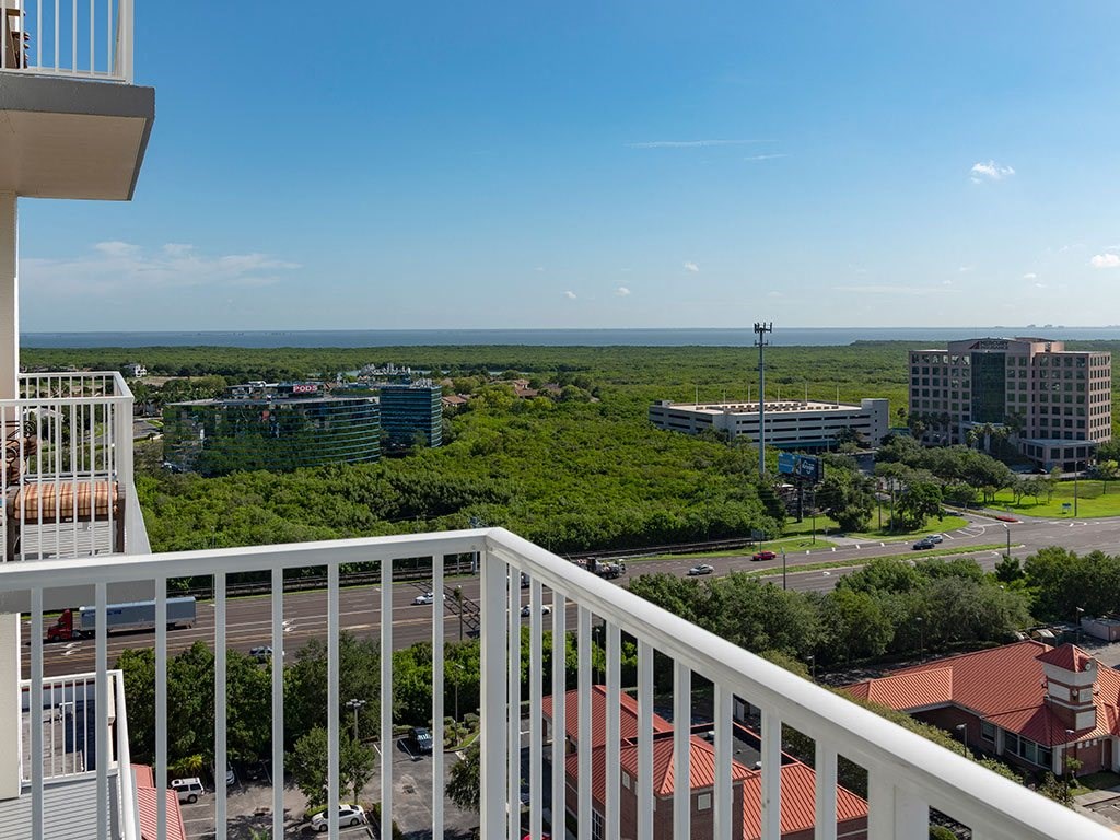 A balcony overlooks a cityscape with buildings, roads, and greenery.