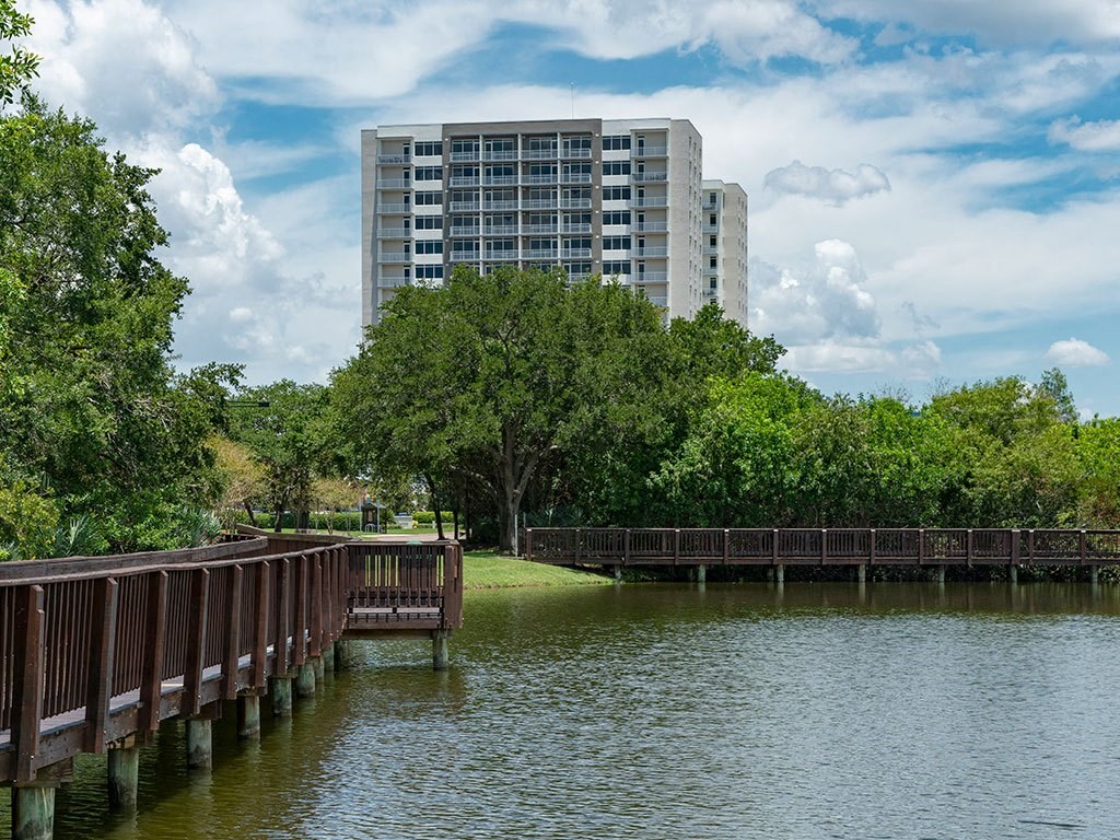 A wooden pier extends into a lake with a large building in the background.