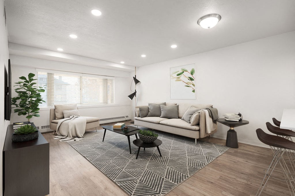 Living room with light fixture, hardwood flooring, white walls, and windows with blinds