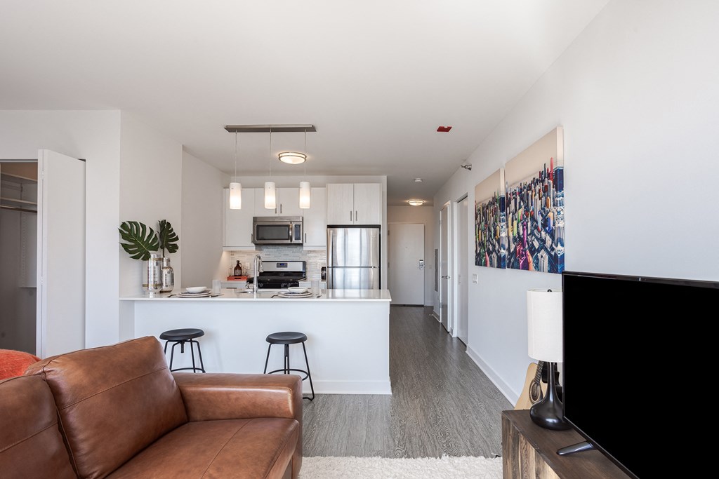A brown leather couch is in the foreground of a modern kitchen and living room.