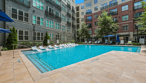 A swimming pool surrounded by lounge chairs and umbrellas in front of a building.
