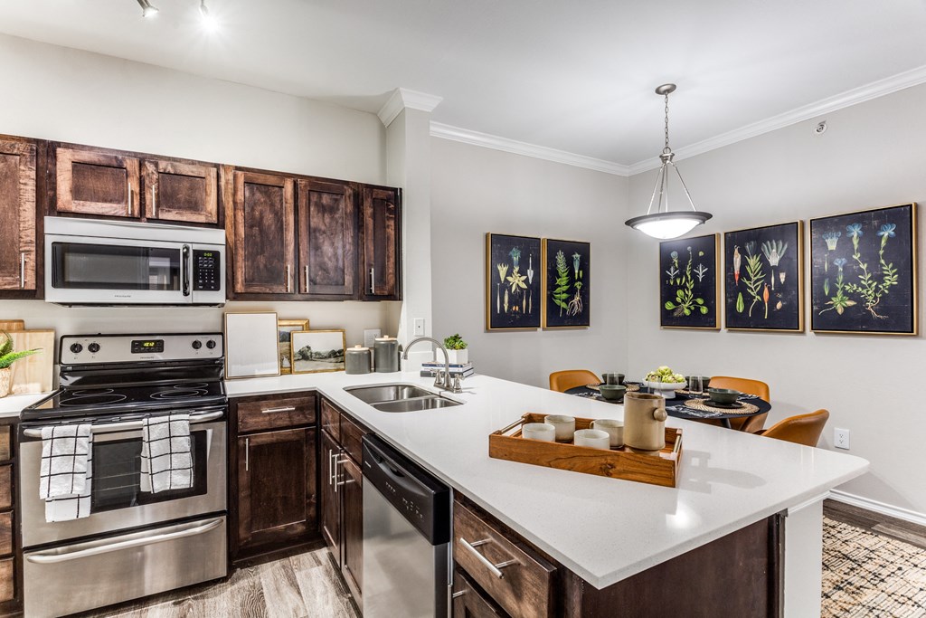 3 Bedroom Apartments in North Austin, TX - Sycamore Springs - Modern Kitchen with Quartz Counters, Wooden Cabinetry, Stainless Steel Appliances, a Dining Area, and Faux Plank Flooring 