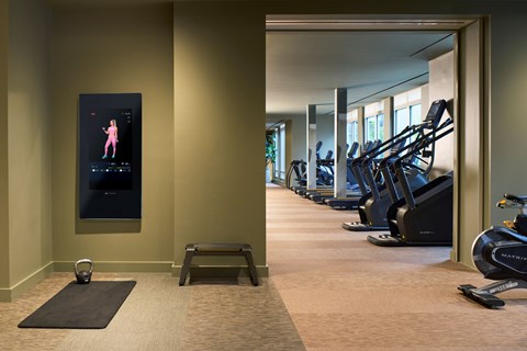 A gym with a row of treadmills and a woman on a screen.
