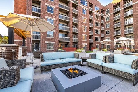 A patio with a fire pit and seating area in front of a brick building.