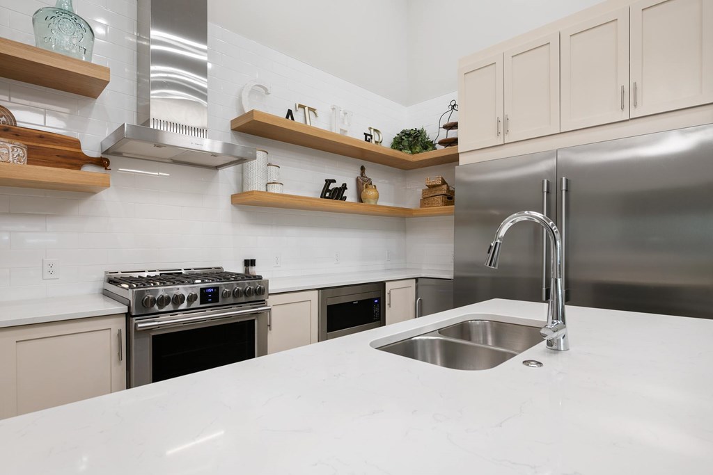 A modern kitchen with a stainless steel refrigerator, a white countertop, and wooden shelves above the stove.
