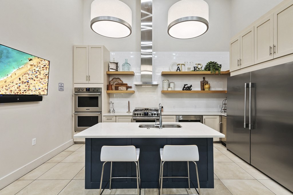 a kitchen with white cabinets and a blue island with two white chairs