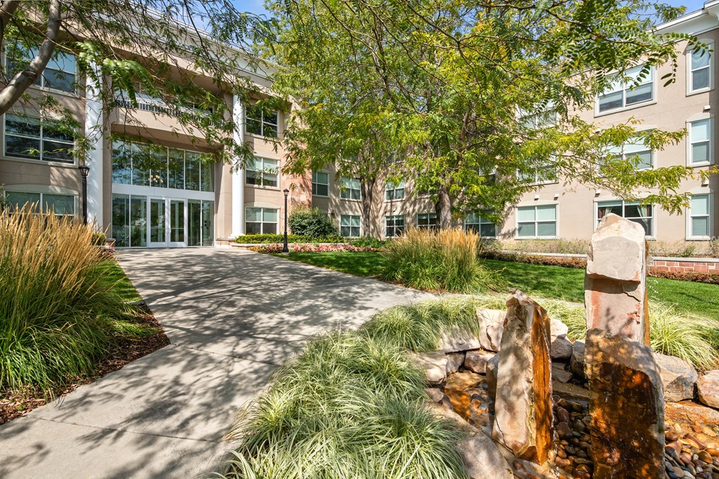 A pathway with a water feature and greenery in front of a building.