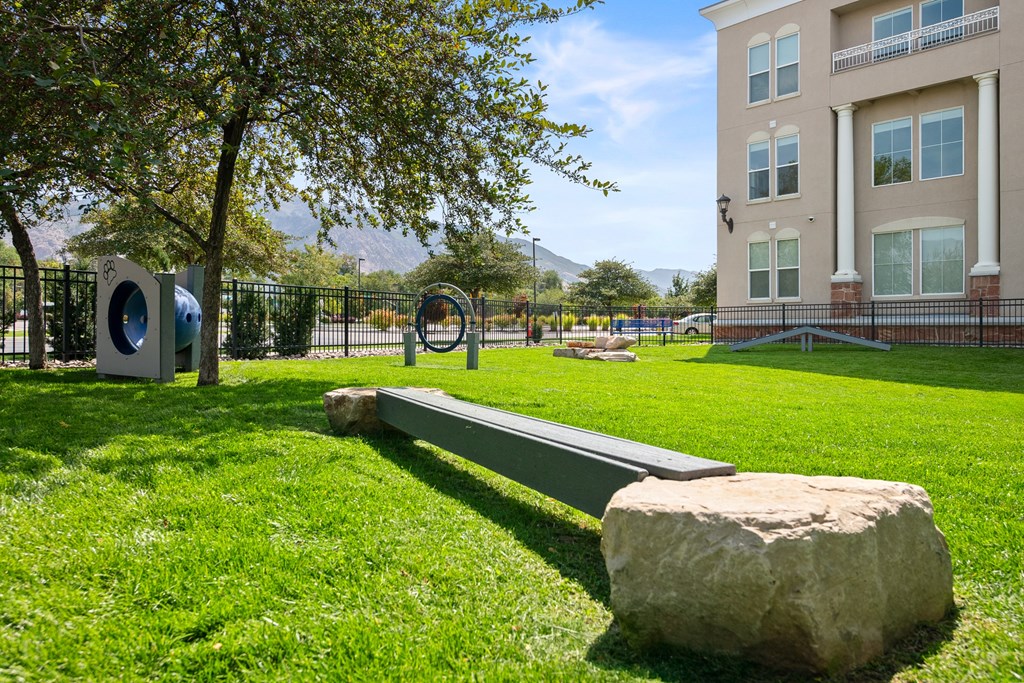 A park with a bench, a rock, and a tree in front of a building.
